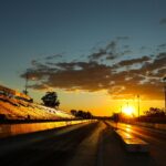 A stunning sunset illuminates an empty racetrack with bleachers, highlighting the sky and track lines.