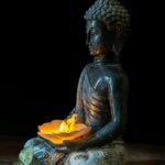 A serene Buddha statue holding a candle, symbolizing peace and spirituality.