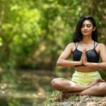 Woman practicing yoga outdoors by a serene water body, embodying peace and mindfulness.