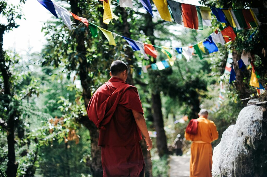 Buddhist monks walking under vibrant prayer flags in a serene forest in Nepal.
